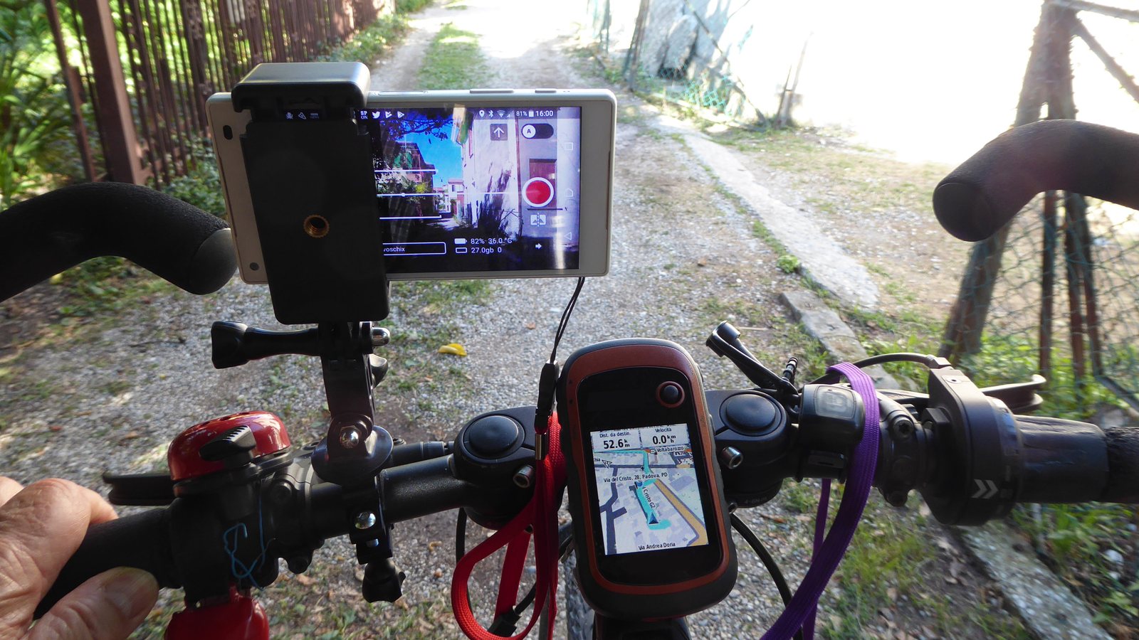Smartphone et GPS fixés sur le guidon d'un vélo par deux supports à collier, sur un chemin de gravier