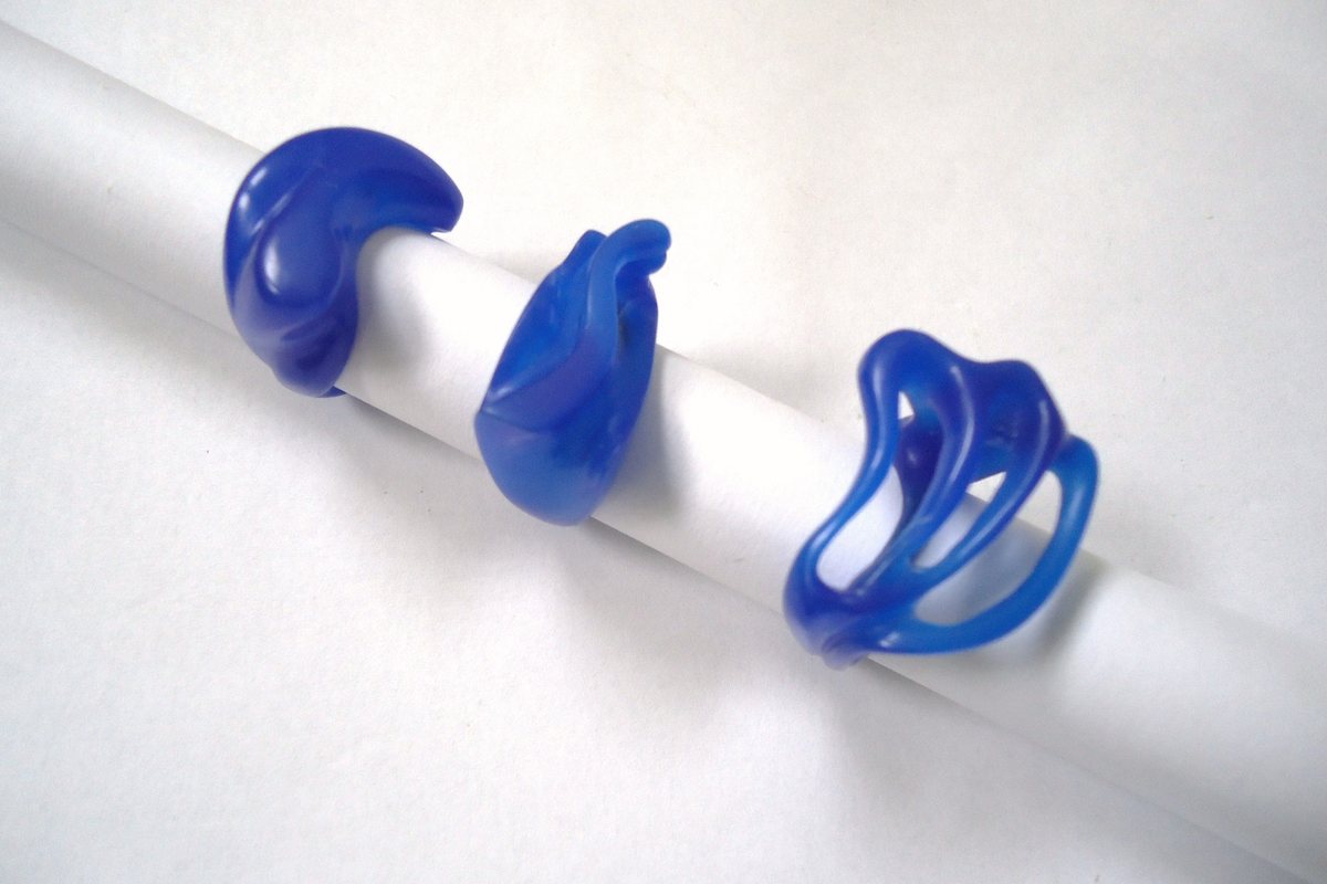 Trois modèles de bagues en cire bleue enfilés sur un tube blanc, l'un d'eux ajouré, avant la fonte