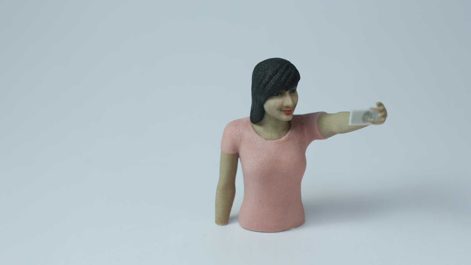 Figurine en couleur d'une femme en train de prendre un selfie, imprimée en 3D d'après une personne réelle, sur fond gris clair