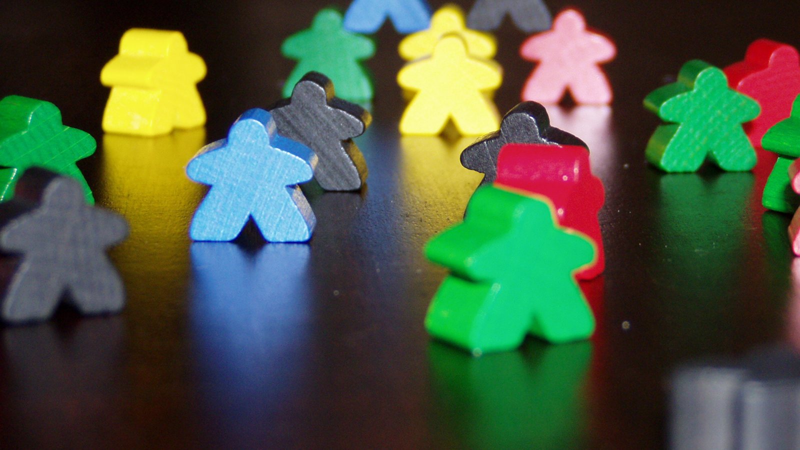 Meeples en bois de six couleurs sur une table sombre, la silhouette de pion que l'on reproduit en PLA pour un prototype