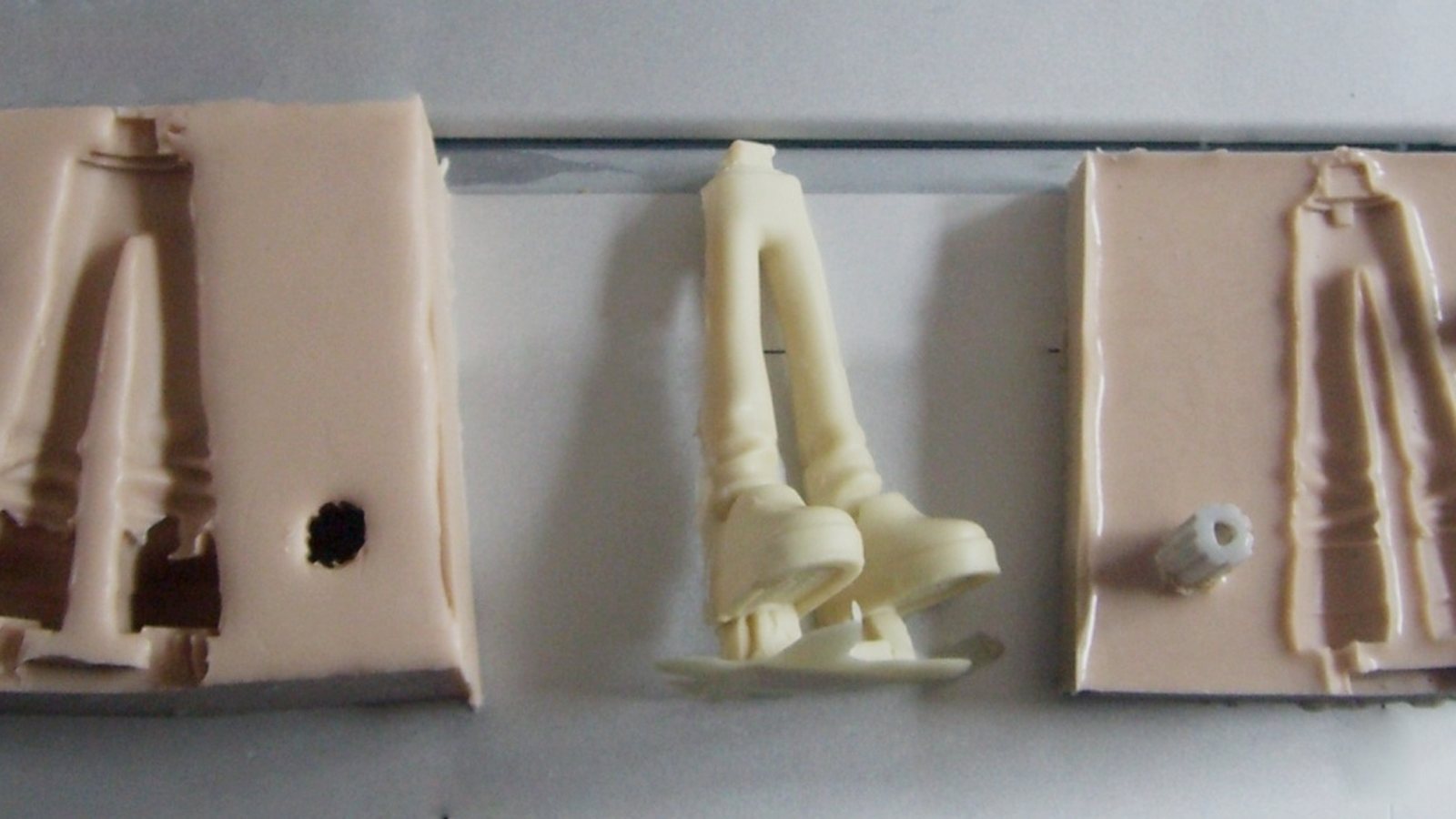 Moule en silicone en deux moitiés ouvertes, avec le canal de coulée et une clé de centrage, et le tirage en résine crème posé entre elles