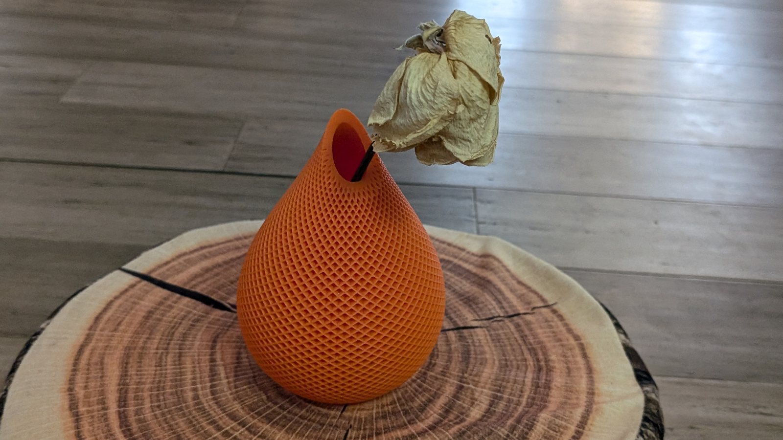 Vase orange imprimé en 3D à motif de losanges ajourés, posé sur une rondelle de bois avec une rose séchée