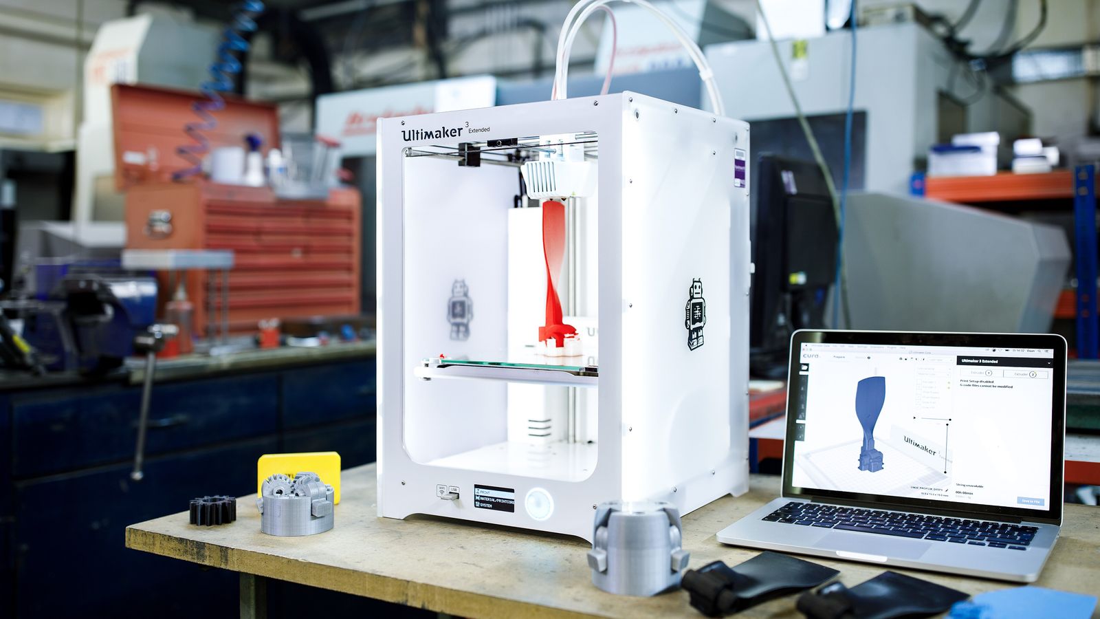 Imprimante 3D à filament sur un établi d'atelier, entourée de pièces de prototype imprimées