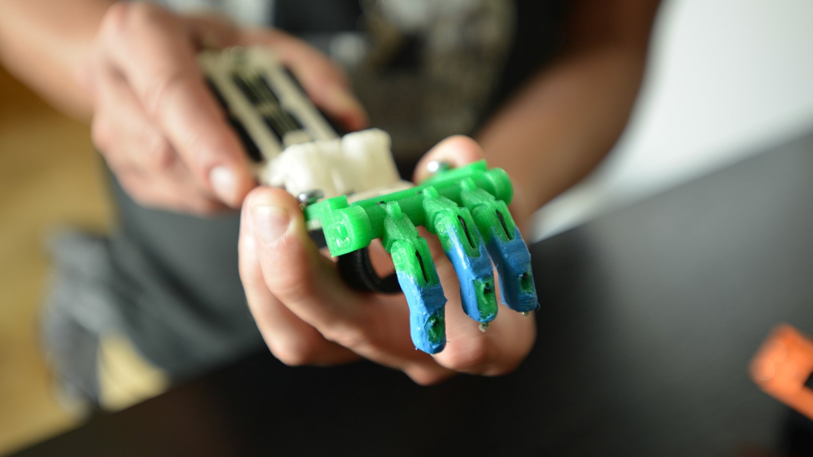 Prototype imprimé en 3D en filament vert, bleu et blanc, tendu dans la paume pendant une démonstration