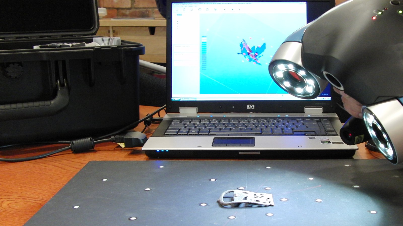 Scanner 3D portatif qui numérise une petite pièce métallique posée sur un plateau à cibles, maillage affiché sur l'ordinateur