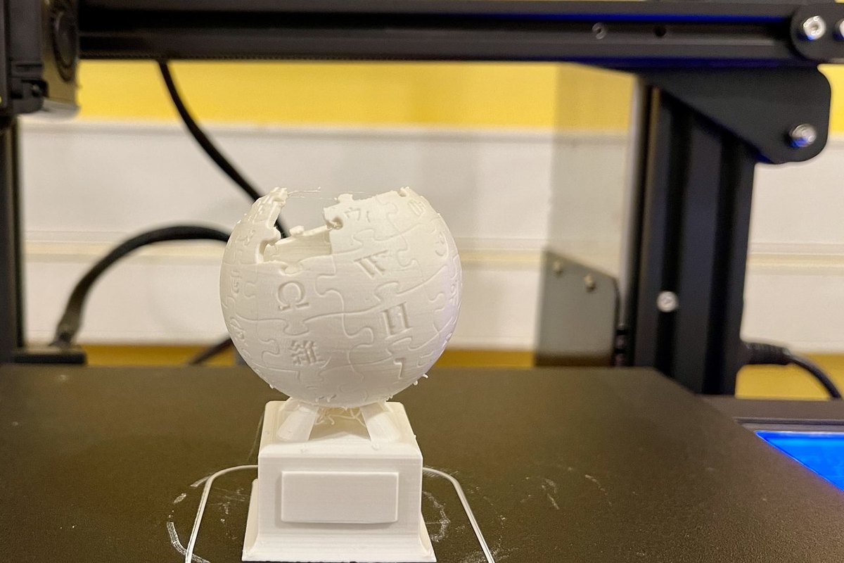 Trophée en PLA blanc qui vient de sortir d'une imprimante 3D à filament, encore sur le plateau avec sa bordure d'adhérence