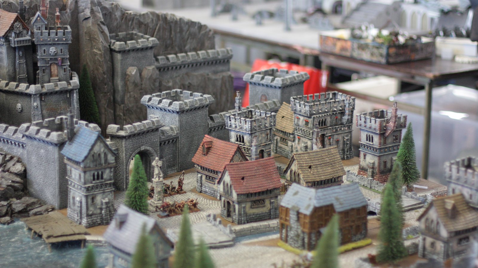 Table de wargame fantasy couverte de décors peints : remparts, tours crénelées et maisons à toits de tuiles à l'échelle des figurines