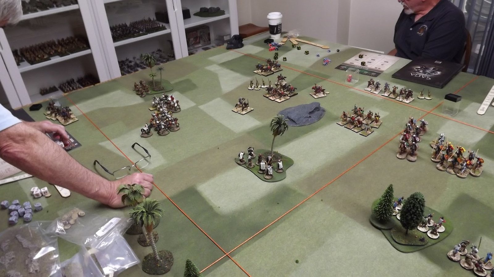 Partie de wargame historique sur une table en feutrine avec bosquets, palmiers et régiments de figurines soclées